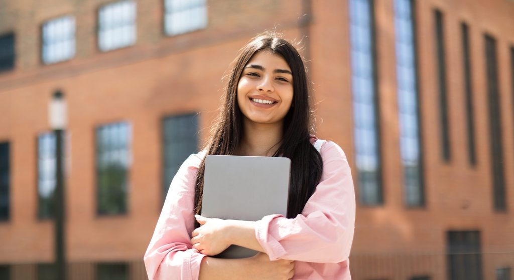 Young hispanic student standing in front of her school